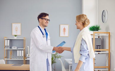Fototapeta premium Smiling male therapist doctor in white medical uniform with stethoscope meeting female patient in clinic, satisfied pleased client woman excited by good medical service in clinic, healthcare help
