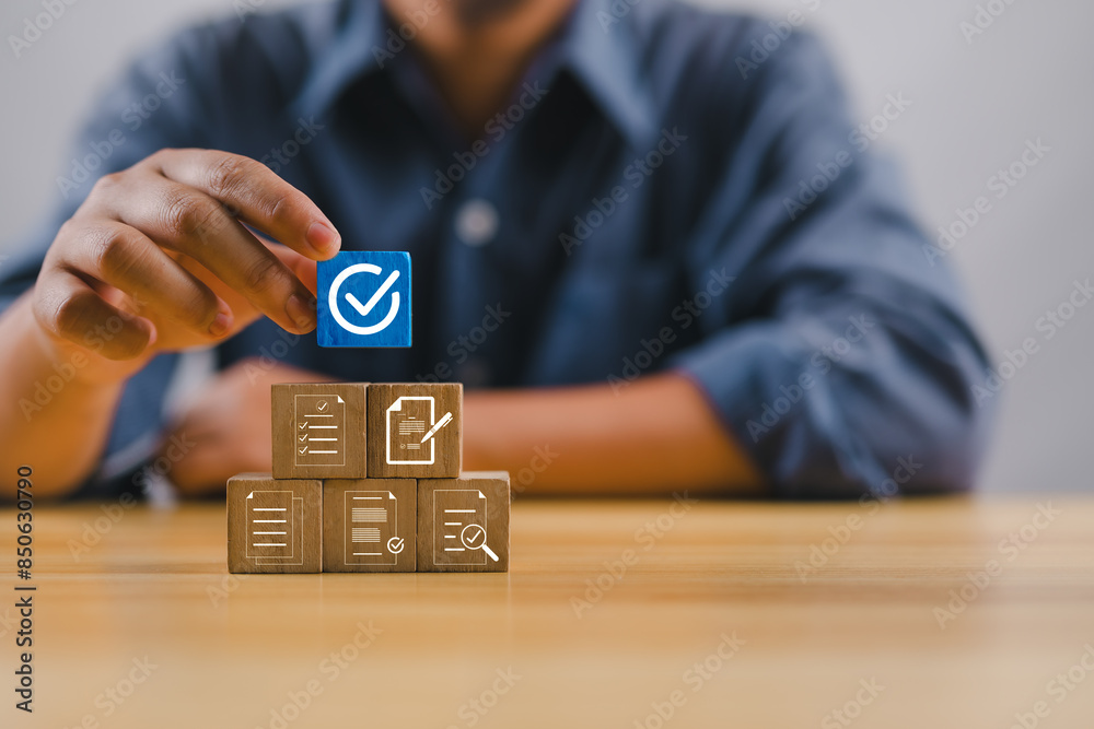 Poster Hand holding white correct sign mark on blue wooden block cube and the top of document icon for ISO quality control certification and project approval concept..