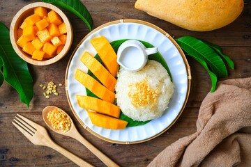 Mango and Sticky Rice on banana leaf with white plate and coconut milk wooden blackground, top view food table	