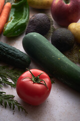 A ripe red tomato next to a green zucchini and a cedar branch