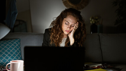 Stressed woman working late at home with laptop, paperwork, and coffee, showing fatigue and...
