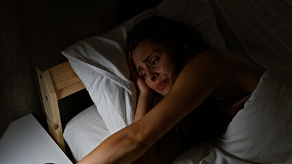 A distressed woman lies awake in a dark bedroom, evoking themes of insomnia, stress, and worry.