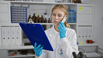 A focused young woman scientist multitasking in a laboratory while speaking on the phone and...