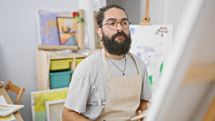 Fototapeta premium A young bearded hispanic man focused on painting in a bright art studio, exuding creative energy and artistic flair.