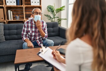 Shocked senior man in medical mask covering mouth with hand, surprised silence expression. afraid in psychology clinic, fear of speaking out.