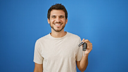 A cheerful young hispanic man holding car keys stands against a solid blue background, exuding confidence and satisfaction. © Krakenimages.com