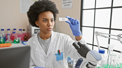 A focused african american woman scientist analyzes a slide in a laboratory setting, demonstrating expertise and precision.