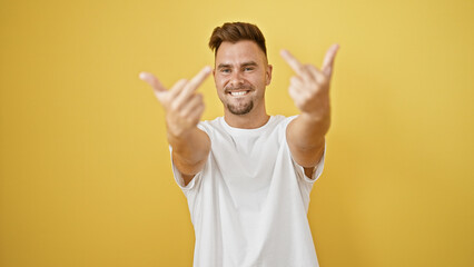 Smiling young man giving the middle finger isolated against a vibrant yellow background, depicting...