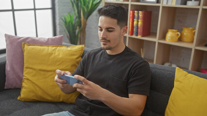 Obraz premium A young hispanic man with a beard plays a video game in the living room of his apartment.