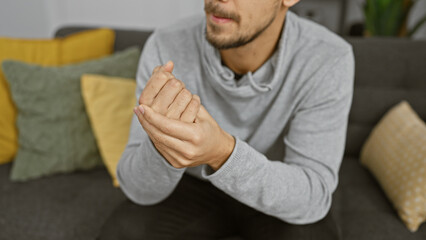 Fototapeta premium Pained young hispanic man holding wrist in a modern living room