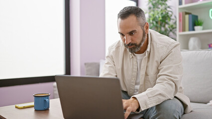 Senior hispanic man with beard working on laptop in living room