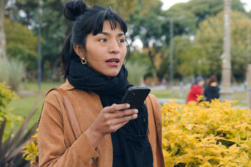 Young Native Latin American Woman of Bolivian Ethnicity in a park sending a voice note on the phone