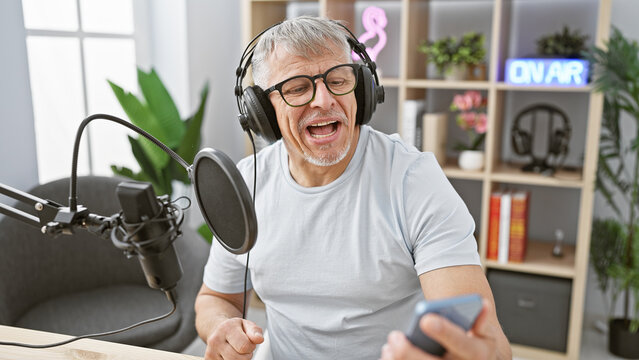 Happy senior man with headphones singing passionately in a modern radio studio.