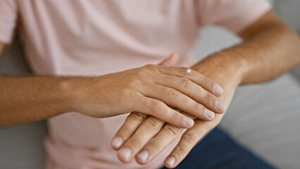 Hispanic man applying cream to his hands indoors for skin care routine at home.
