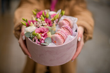 Hands of the young woman with a flowers and macarons in a box on a blurred background