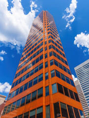 Stunning Urban Photography of a Vibrant Orange Skyscraper Under a Bright Blue Sky with White Clouds, Capturing Modern Architectural Beauty in a Bustling Cityscape