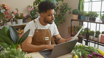 African american man reading document in a flower shop surrounded by various plants indoor.
