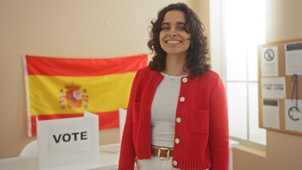 Young hispanic woman voting in a spanish electoral college room with flag and vote sign in the background.