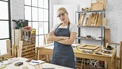 Confident woman carpenter in workshop with arms crossed wearing safety glasses