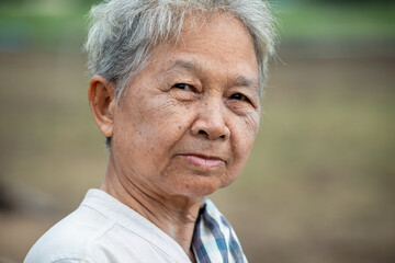 An elderly Asian grandmother in her 70s with white hair and wrinkled skin looks at the camera, close-up