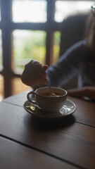 A woman stirs a cup of coffee in a cozy indoor setting, hinting at a relaxed or contemplative moment.