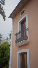 A quaint mediterranean-style house with a balcony, door, tropical foliage, and vintage lamp in a tranquil residential setting.