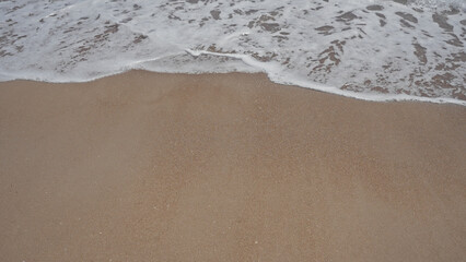 A serene beach scene showing gentle waves on the sandy shore under a clear sky.