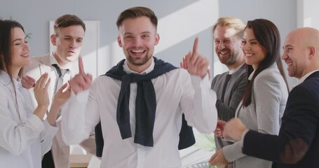 Team of young positive office workers celebrates success, a successful deal, or victory, giving high fives, applauding, and dancing in a good mood during a business meeting in modern office.