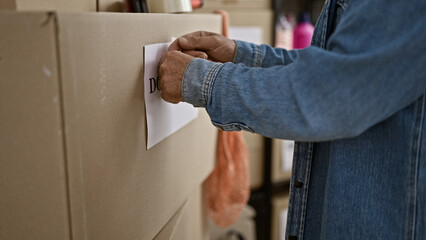 Senior man attaching document to cardboard box in a warehouse, depicting logistics or organization.