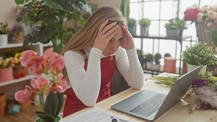 Stressed young woman florist with laptop in flower shop looking overwhelmed