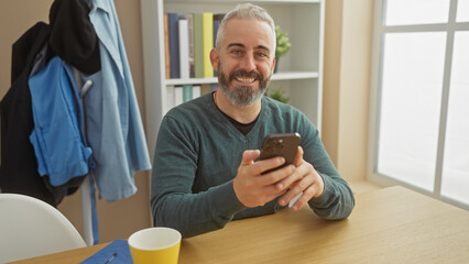 Caucasian bearded man smiling while holding smartphone at home
