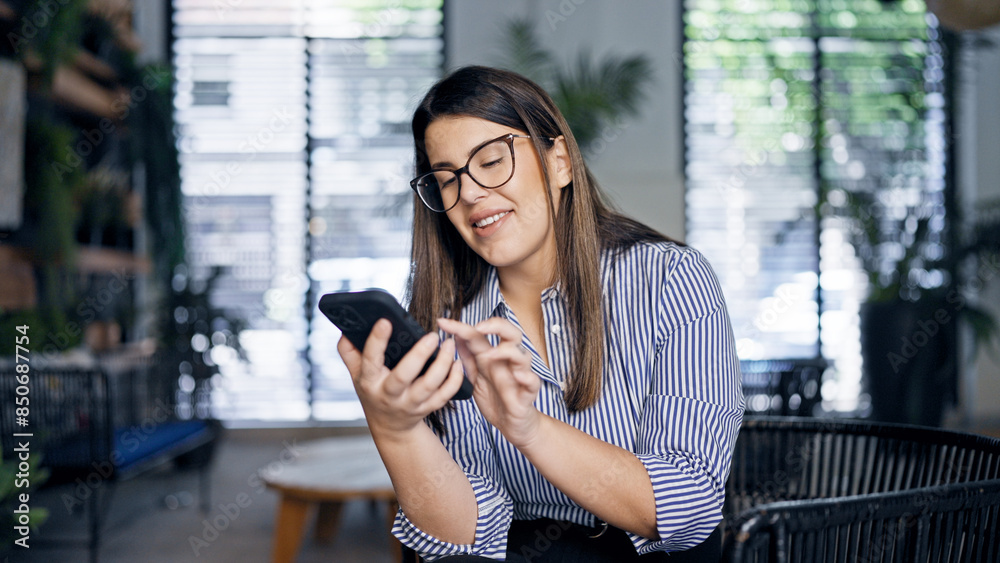 Sticker Young beautiful hispanic woman using smartphone sitting on a chair at the office