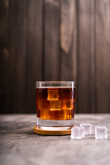 Whiskey, bourbon or cognac on glass with ice cube on a rustic wooden background with copy space
