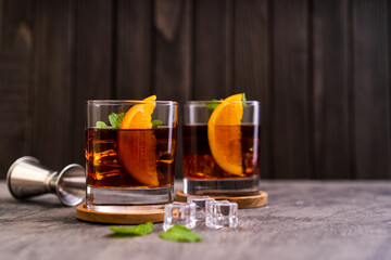 Fresh made Cuba Libre cocktail with ice cube, rum, cola, mint and lemon on wooden background