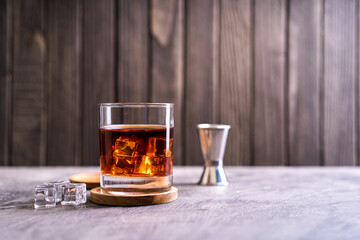 Whiskey, bourbon or cognac on glass with ice cube on a rustic wooden background with copy space
