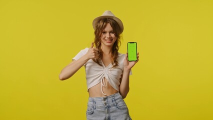 Young woman in casual shows thumb up holds smartphone chroma key green screen. Travel, summertime vacation, tourism leisure concept.