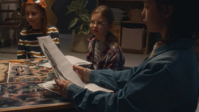 Side footage of little boy giving character sheet to girl while playing tabletop game at home in evening