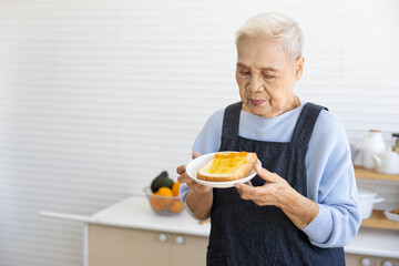 senior housewife eating bread toast with orange jam in the kitchen