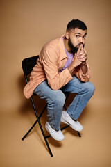 Handsome man in chair, hand on mouth, deep in thought.