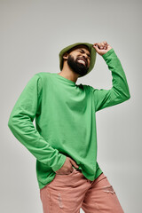 Fototapeta premium Stylish African American man with beard in green hat posing on vibrant backdrop.