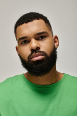 Obraz premium Handsome African American man with a beard confidently posing in a green shirt.