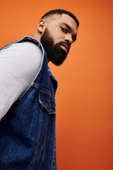 Handsome African American man with beard poses in denim vest on vibrant backdrop.