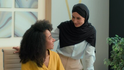 Two happy business women girls diverse multiethnic businesswomen working office Arabian muslim islamic female boss leader in hijab teach help African American student mentor teamwork friendly smiling