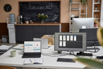 Modern office desk setup equipped with laptop displaying page of calendar and computer with app design program on screen. Functional workspace for remote learning or working, copy space