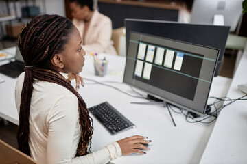Side view of multiethnic female working on desktop computer developing new app design at modern office table, copy space