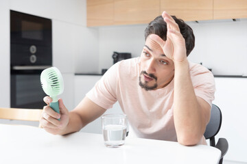 Tired and overheated man suffering from a heat attack uses an electric handy fan to cool himself down in a hot summer day © Vitaliy