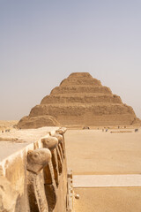 The step pyramid of Djoser In Saqqara, Egypt with stone carved cobra snakes in the foreground