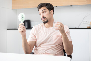 Tired and overheated man suffering from a heat attack uses an electric handy fan to cool himself down in a hot summer day © Vitaliy