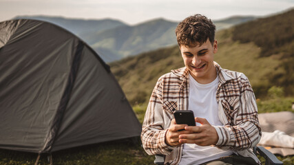 Young boy sit in front tent and use mobile phone on the mountain