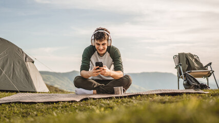 Young boy sit on blanket on the mountain listen music on headphones